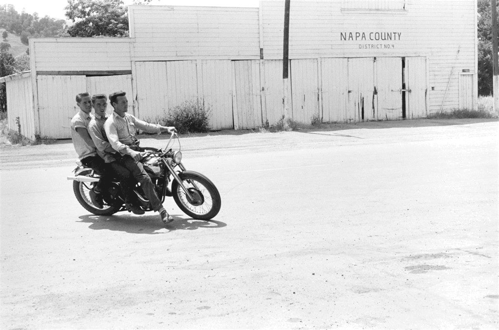 Three young men on a motorcycle beside a Napa County building